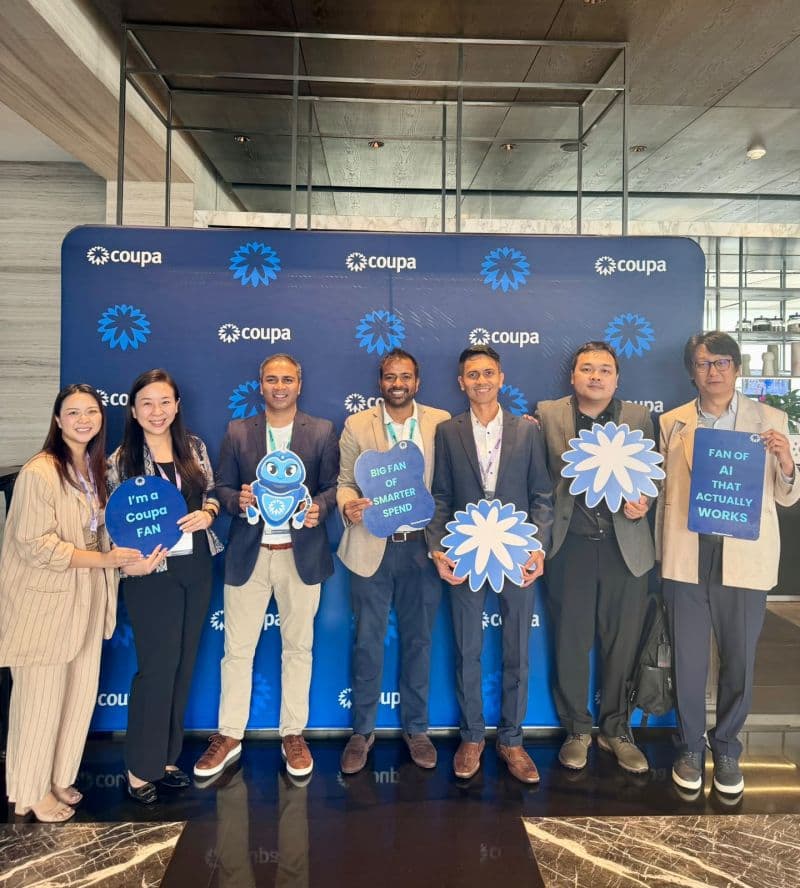 Seven attendees posing with Coupa-themed signs in front of the Coupa backdrop at Coupa Connects Jakarta.